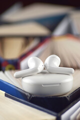 Small white headphones against a background of many books. Audiobook concept