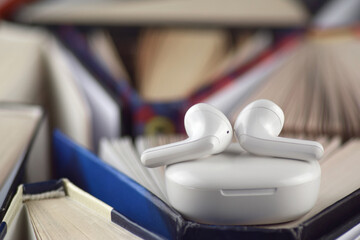 Small white headphones against a background of many books. Audiobook concept