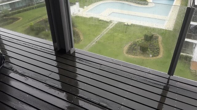 Balcony view of a rainy landscape with a pool and trees