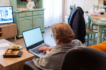 Senior woman at home enjoying using the laptop sitting on a armchair
