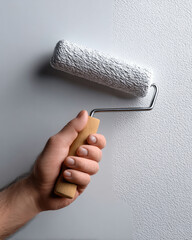 Hand holding paint roller applying white paint on textured wall, home improvement concept, close up, clean and fresh atmosphere