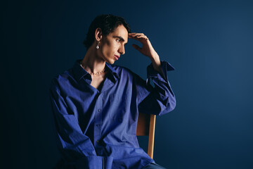 Handsome man in stylish blue outfit poses thoughtfully against a deep blue backdrop
