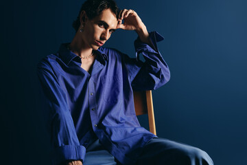 Stylish man in blue shirt poses thoughtfully against a deep blue background