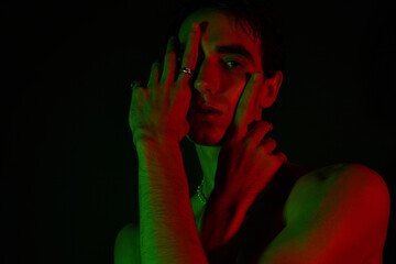 Stylish man posing dramatically in vibrant green and red lighting against a dark backdrop