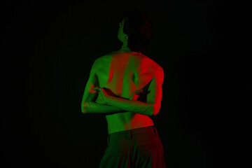 Stylish man poses creatively against a dark background with vibrant lighting