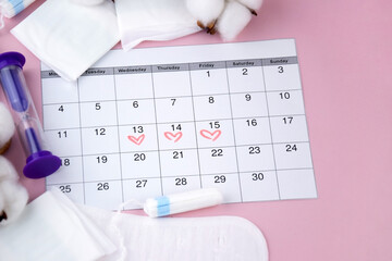 Women's menstrual pads, tampons, female menstruation calendar and alarm clock on a pink background.