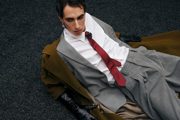 Stylish man in elegant gray suit and bold red tie lounging on dark floor