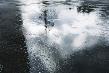 Top-down view of a wet concrete floor featuring rain puddles reflecting the cloudy sky. Realistic water texture on rough surface.