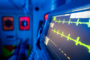 Selective focus on monitor of vital signs against patient on stretcher inside ambulance car of emergency medical service at night. Themes rescue, urgency and health care.