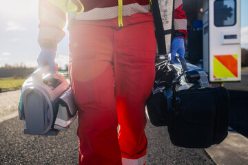Emergency medical service. Paramedic hand in blue surgical gloves while running with defibrillator monitor and other equipment against ambulance car. Themes rescue, urgency and health care.