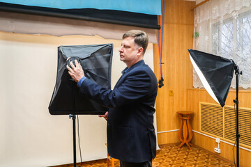 Photographer turning on softbox lighting equipment in a professional photo studio setup for portrait or product photography.