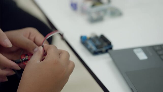 Hands connecting jumper wires to a microcontroller board for an educational robotics project, part of STEM or Arduino learning activity.