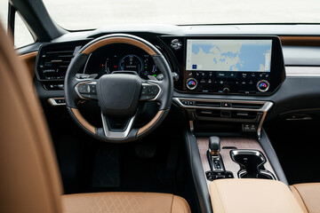 A premium, modern brown car interior, leather steering wheel, large navigation screen, air ducts, deflectors on the car panel. Interior details.