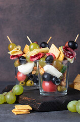 Jarcuterie in two glass includes various types of sausages, pickles, cheese, nuts, vegetables and fruits