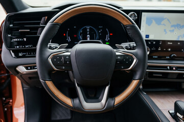 A premium, modern brown car interior, leather steering wheel, large navigation screen, air ducts, deflectors on the car panel. Interior details.