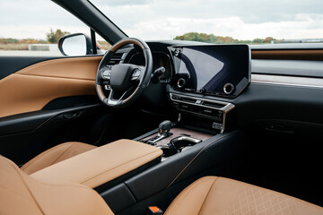 Fototapeta premium A premium, modern brown car interior, leather steering wheel, large navigation screen, air ducts, deflectors on the car panel. Interior details.