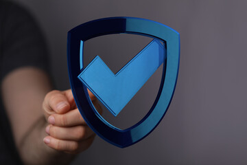 A person's hand presenting a digital shield icon with a checkmark indicating protection, security, and approval in cybersecurity and