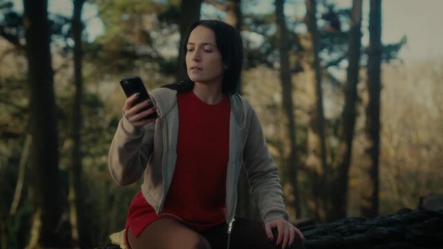  a young woman hiking in a forest as she video calls with her smartphone. With a bright smile and a backpack, she captures the moment amidst the natural scenery, reflecting the joy 
