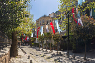 Istanbul, Turkey, 23 May 2025, Sunny cobblestone street lined with trees and hanging flags, showing a quiet neighborhood scene. Cihangir district