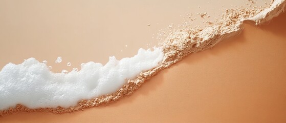 Close up of gentle ocean wave with white foam washing over fine sand on a pale background.