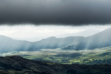 Overlook of a vast valley in County Kerry, Ireland with sun rays and clouds.