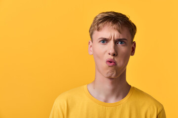 Fototapeta premium Male figure in a yellow shirt against a bright yellow background making a puckered lips expression, studio style with bold color, playful mood, expressive emotion for stock use