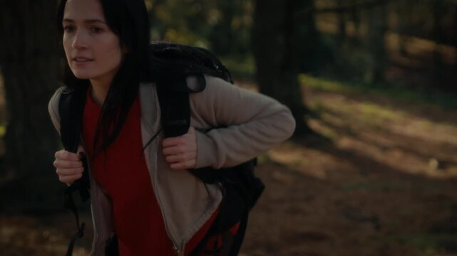  a young woman hiking in a forest, showcasing her determination and connection to nature, looking up as she walks along a trail surrounded by trees and dappled sunlight.