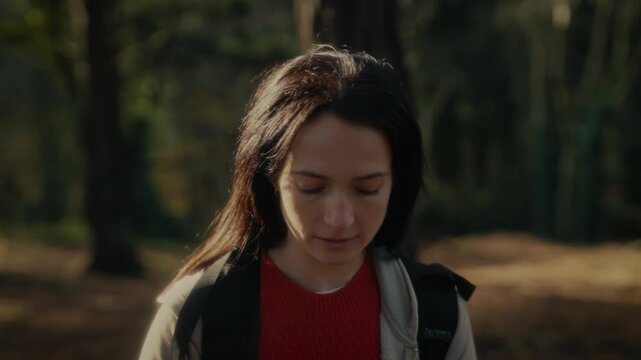  a young woman hiking in a forest, showcasing her determination and connection to nature, looking up as she walks along a trail surrounded by trees and dappled sunlight.