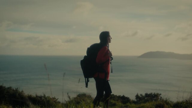  a young woman standing at a scenic viewpoint, gazing out over a tranquil body of water and distant hills. With her backpack slung over her shoulders.