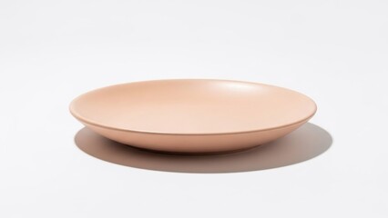 A light peach-colored ceramic bowl stands empty on a white surface, casting a subtle shadow underneath it
