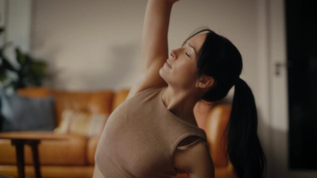 woman practising yoga in a cosy living room setting. She is in a lunging pose on a yoga mat, with a tablet in front of her displaying a workout or meditation session. 