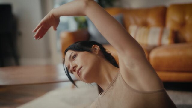 woman practising yoga in a cosy living room setting. She is in a lunging pose on a yoga mat, with a tablet in front of her displaying a workout or meditation session. 