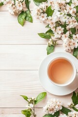 White blossoms and green leaves arranged on light wood surface with cup of warm beverage.