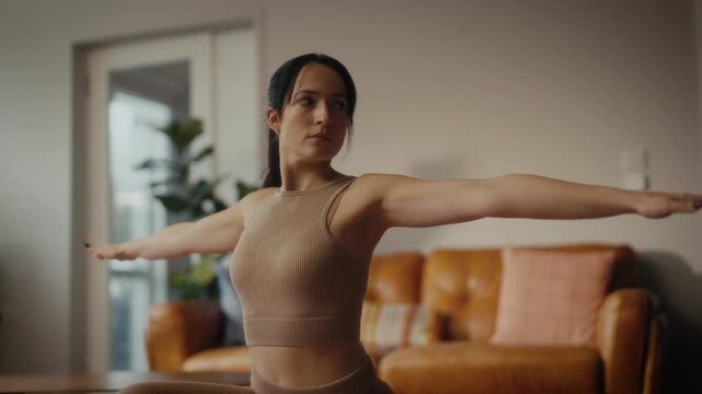 woman practising yoga in a cosy living room setting. She is in a lunging pose on a yoga mat, with a tablet in front of her displaying a workout or meditation session. 