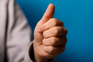 A close-up of a hand with the thumb up on a vibrant blue background, conveying approval and...