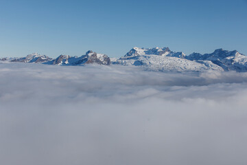 Obraz premium Majestic snow-covered mountains towering above a sea of clouds under a clear blue sky. A stunning la