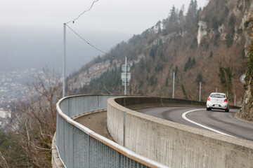 A white car drives along a winding road with a concrete barrier against a mountain background in mis © vegefox.com