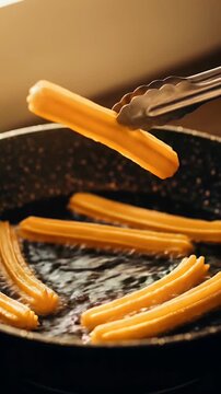 Tongs lift a hot, golden churro dripping oil from a pan