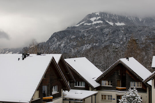Scenic winter view of houses with snow-covered roofs and mountain background. - Powered by Adobe