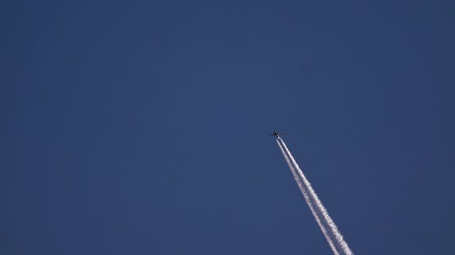 Passenger airplane flying high in a clear blue sky, leaving a long white vapor trail behind