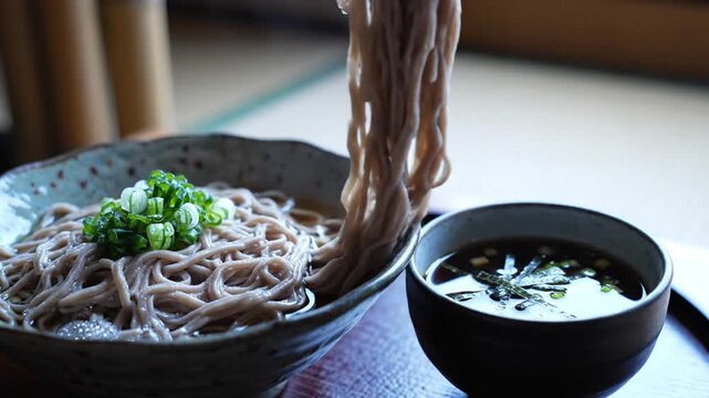 Ceramic bowl of soba noodles with a green onion garnish, lifted strands, and steaming dipping sauce
