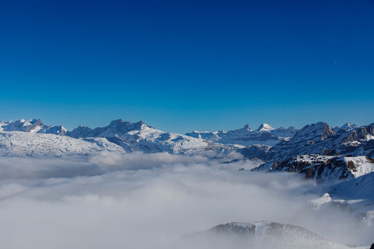 Dramatic landscape of snow-capped mountains and clouds, with a clear blue sky. Winter scenery. - Powered by Adobe