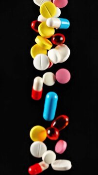 Colorful pills and capsules falling against black background medical pharmaceutical concept