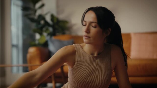 woman practising yoga in a cosy living room setting. She is in a lunging pose on a yoga mat, with a tablet in front of her displaying a workout or meditation session. 