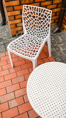 White plastic lattice chair and table on a red brick patio against an orange brick wall outdoors