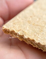 Close Up Of A Rough Brown Cardboard Edge Held By A Person's Finger With Macro Detail Of Fibers And Dust In Soft Natural Light