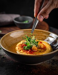 Chef Garnishes Hummus With Microgreens and Spices in a Rustic Bowl With Dramatic Lighting