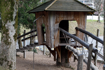 Scenic view of a wooden treehouse with rope bridge on a playground, perfect for childhood memories.