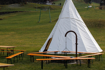 Scenic view of a teepee, benches, and grill in a green field, perfect for outdoor events. © vegefox.com