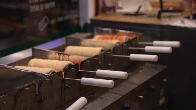 Traditional christmas chimney cake, kurtos kalacs, trdelnik, and polish kołacz slowly rotating and roasting over an open charcoal fire at a festive holiday market